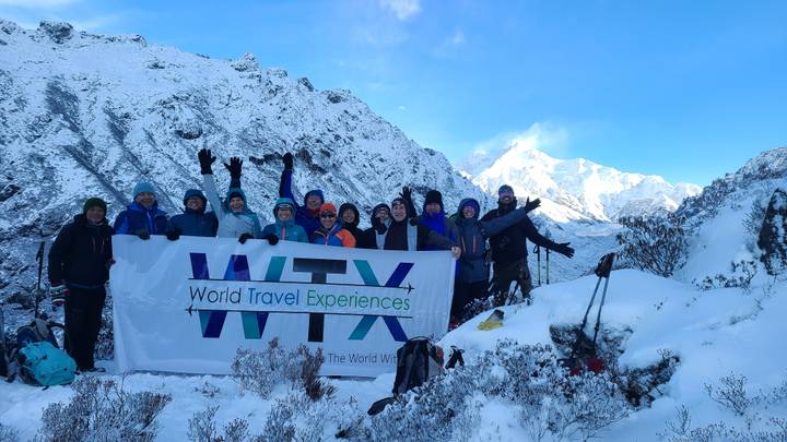 Cheerful trekking group holding 'WTX' banner amid snow-covered Himalayan landscape