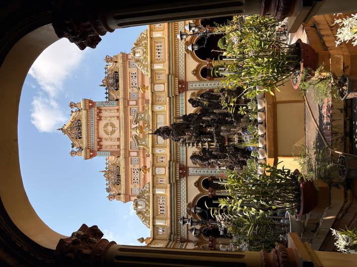 Ornate pastel-colored façade and courtyard fountain of Vinh Trang Pagoda framed by blue sky through an archway.