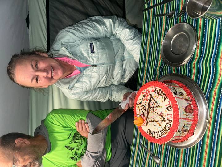 Smiling trekker inside a mess tent about to cut a decorated celebration cake on the Inca Trail.