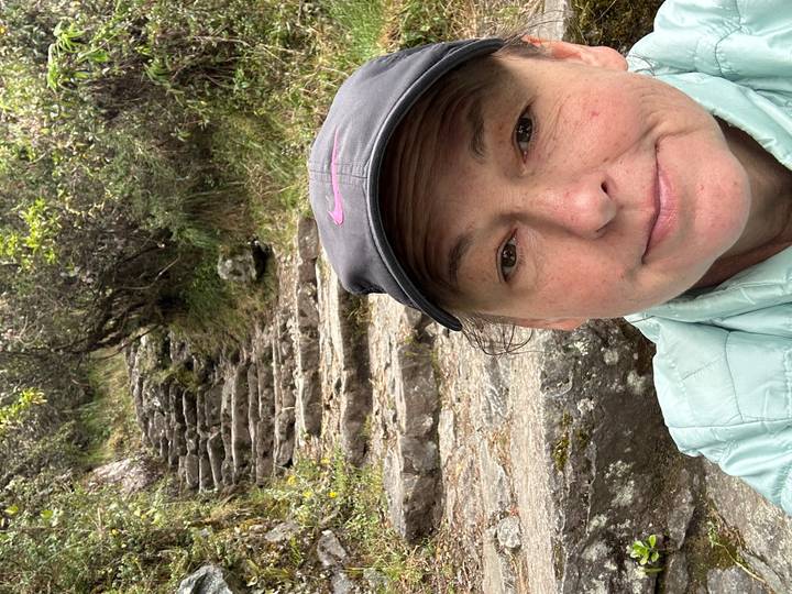 Selfie of a female hiker with stone steps of a lush Andean trail ascending behind her.