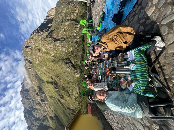 Long outdoor breakfast table set beside towering Andean peaks where trekkers enjoy an early meal at camp.