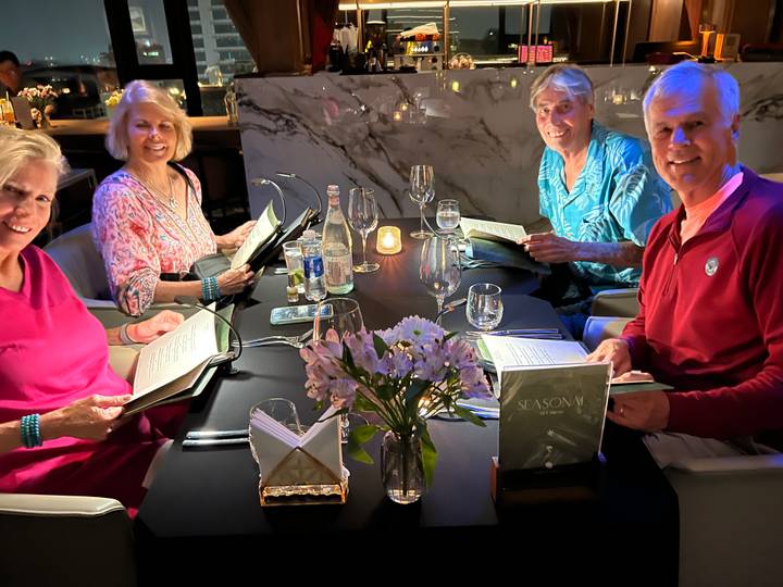 Friends study menus around a candle-lit dinner table in an upscale marble-accented restaurant.