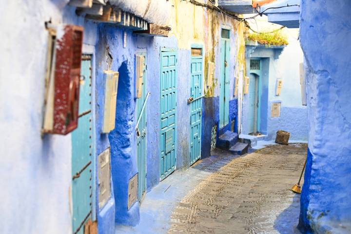 Narrow alley of blue doors and walls in Chefchaouen leading into the medina.
