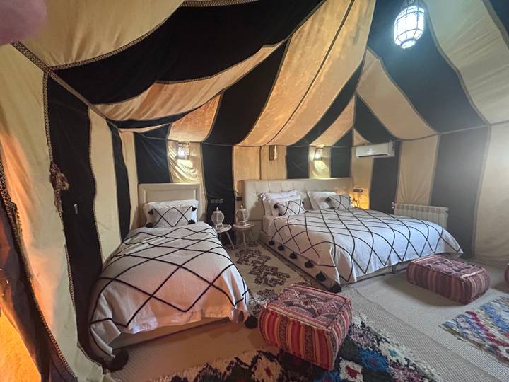 Comfortable desert glamping tent interior with patterned rugs and twin beds beneath canvas roof.