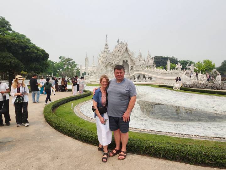 Couple posing in front of the dazzling white facade and reflective pool of Chiang Rai’s White Temple.