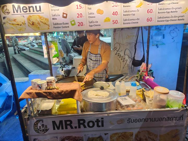 Street-food vendor preparing roti at a brightly lit night stall