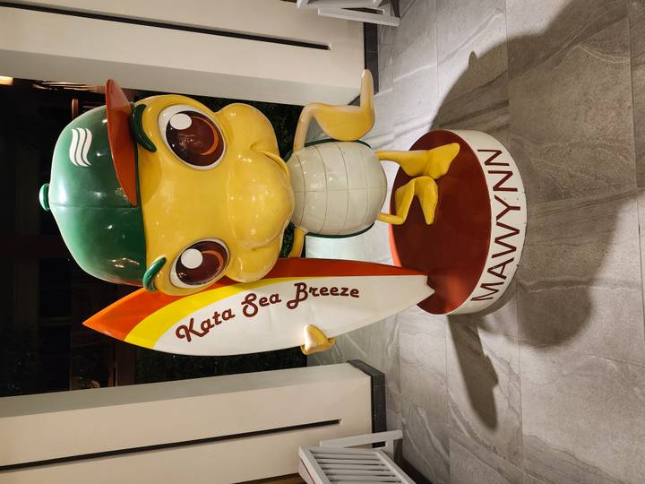 Colorful cartoon turtle statue holding a surfboard labeled 'Kata Sea Breeze'