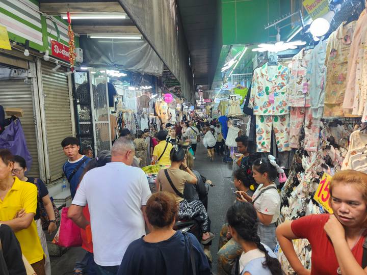 Crowded narrow indoor market aisle packed with shoppers and hanging clothes