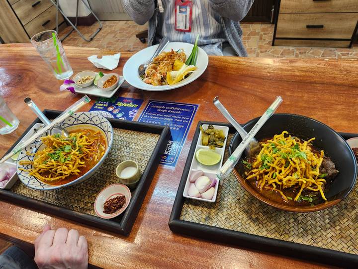 Tabletop spread of Thai dishes including khao soi and pad thai with condiments