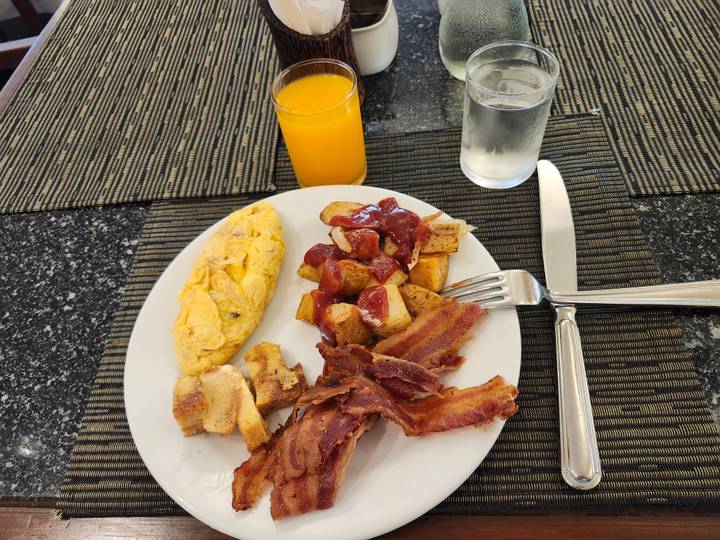 Breakfast plate with omelette, potatoes, bacon and orange juice on dark granite table