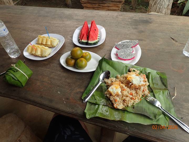 Simple outdoor meal of fried rice wrapped in banana leaf with fruit plates