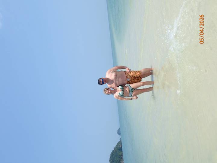 Couple standing in shallow clear sea under bright blue sky with date stamp visible