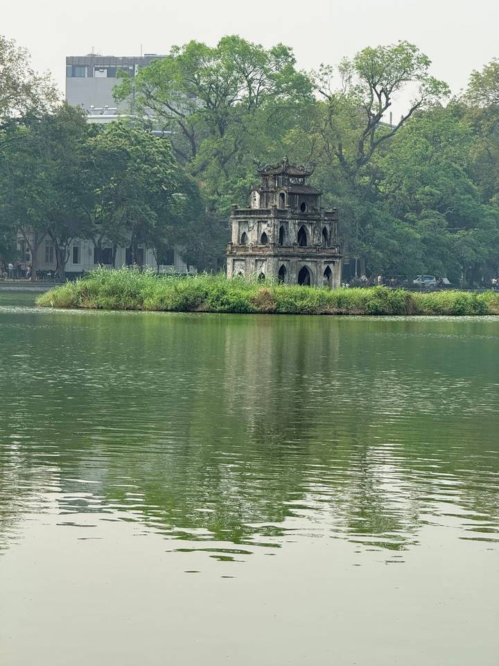 Historic Turtle Tower on small island in Hoan Kiem Lake reflecting in green water