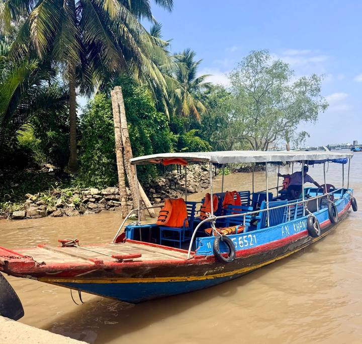 Blue wooden boat with life jackets navigating muddy Mekong Delta waters