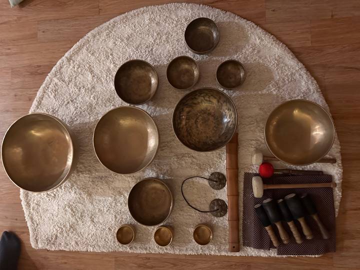 Collection of brass singing bowls and mallets arranged neatly on a circular rug indoors.