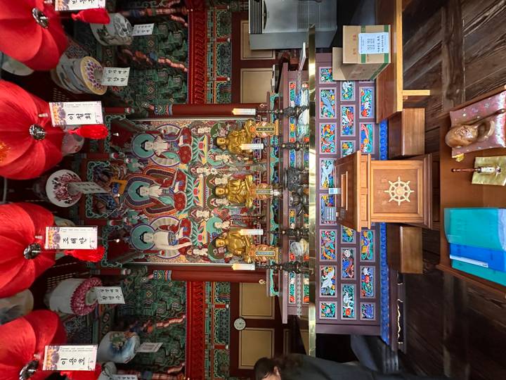Elaborate Buddhist temple interior with colourful murals, golden statues and hanging lanterns.