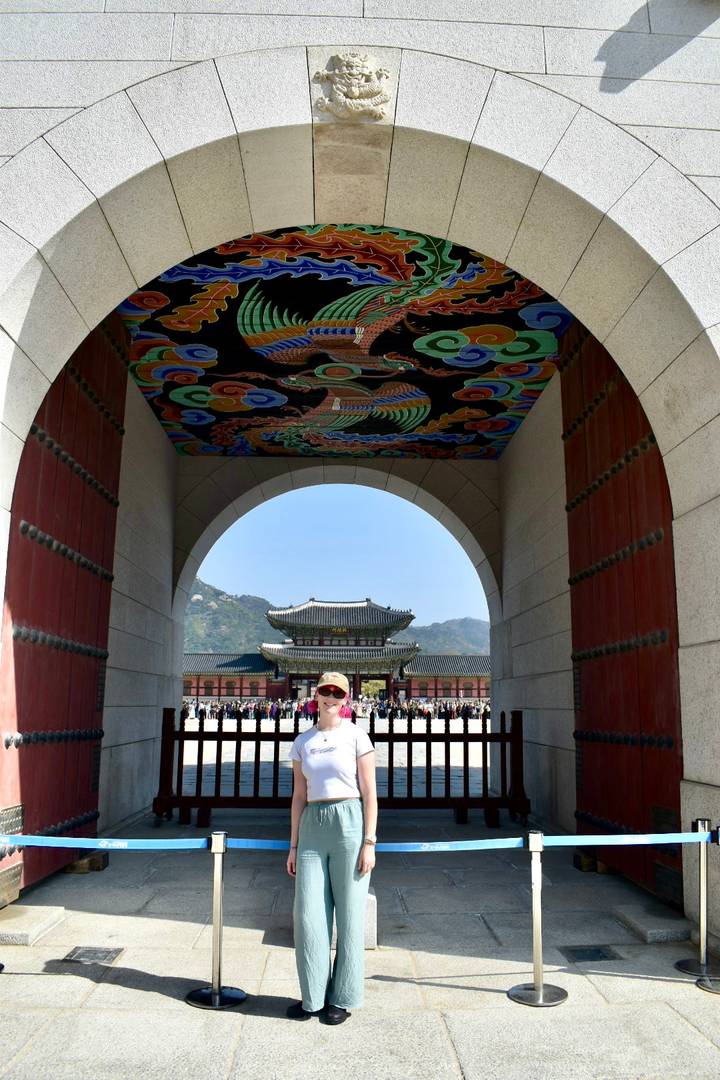 Visitor framed under ornate painted palace archway looking toward main throne hall with mountains behind.