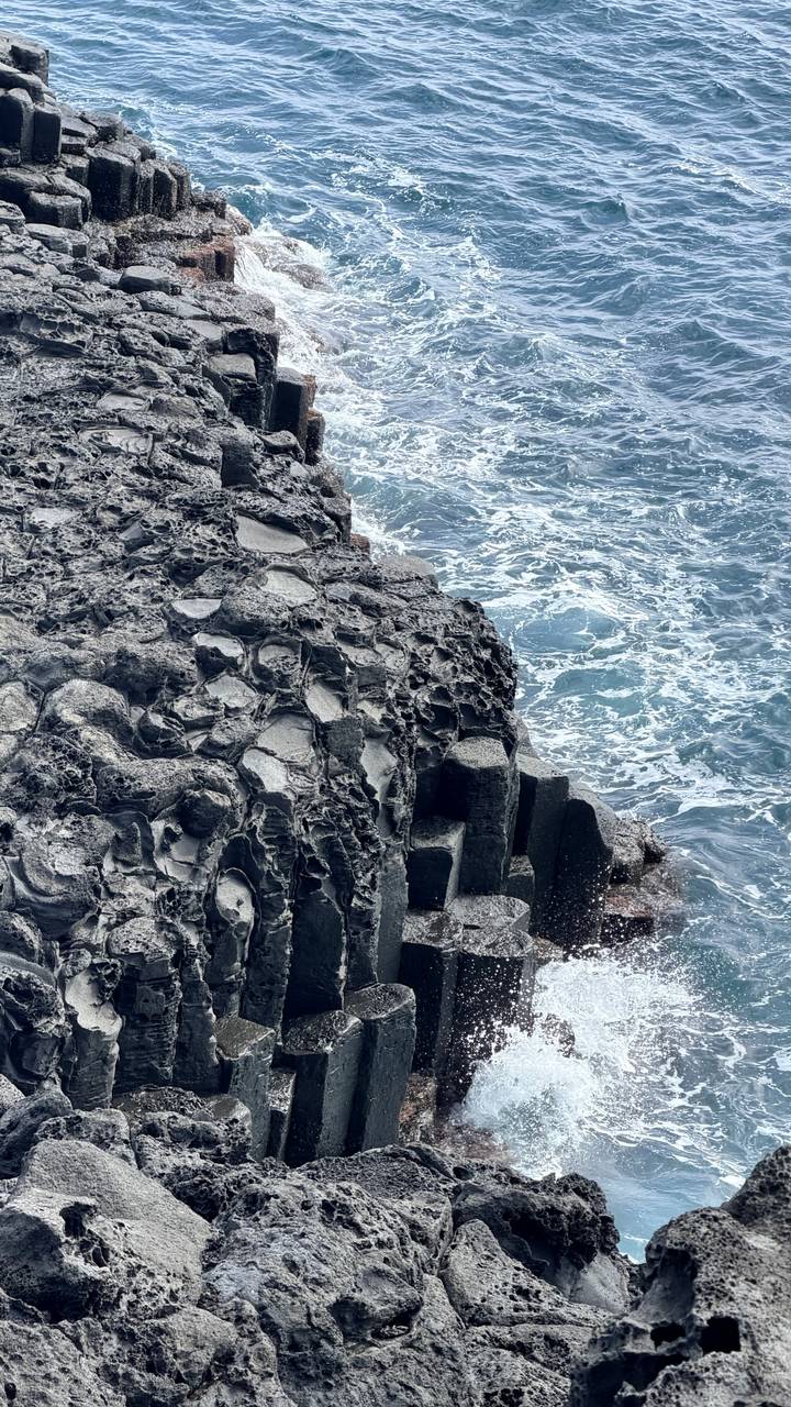Close view of rugged hexagonal basalt cliffs meeting turquoise ocean waves.