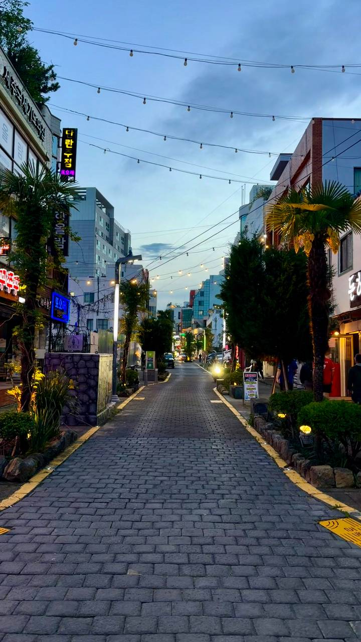 Charming pedestrian alley lined with cafés and neon signs, strung with evening fairy lights.