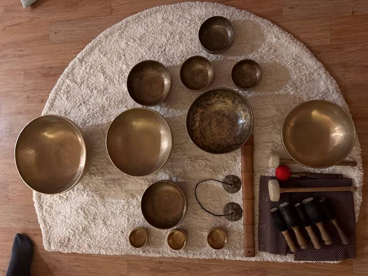 Arrangement of various sized bronze singing bowls and mallets on a circular rug.