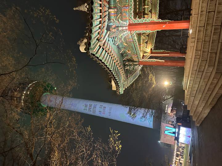 Night view of Busan Tower projection beside a traditional pavilion.