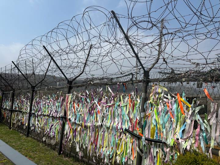 Fence topped with barbed wire and covered in multicolored prayer ribbons at DMZ.
