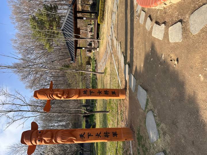 Traditional Korean jangseung totem poles standing beside a stone path in a rural park.
