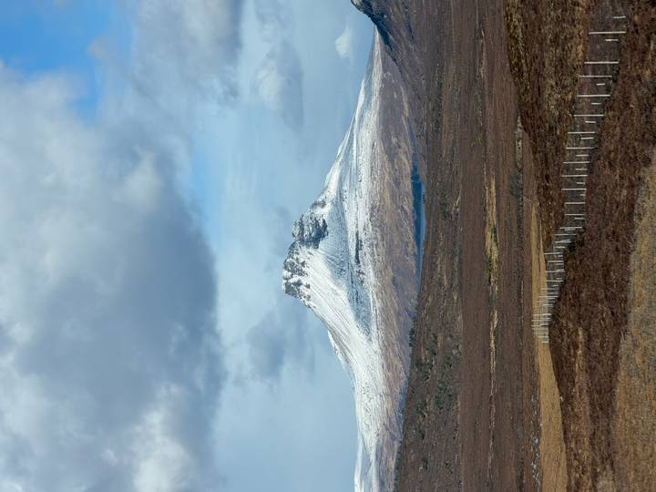 Snow-capped mountain peak rising above moorland under dramatic clouds in the Highlands.
