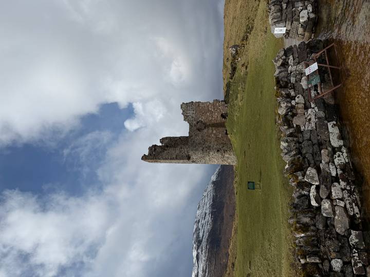 Ruins of Ardvreck Castle against backdrop of snowy hills and moody sky.