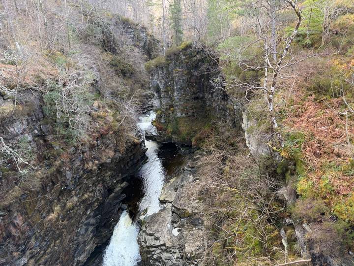 Deep rocky gorge with narrow river cutting through layered stone walls and sparse trees.
