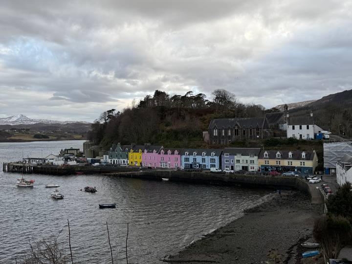 Harbor view of Portree with pastel waterside houses and moored boats under cloudy sky.