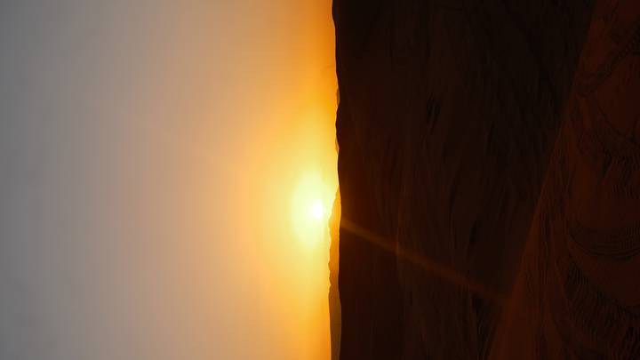 Orange sun setting over rolling desert dunes casting long shadows