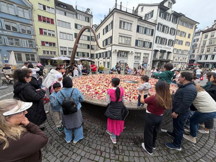 Crowd gathered around a large circular platform filled with colorful rose petals in Zurich’s historic district.