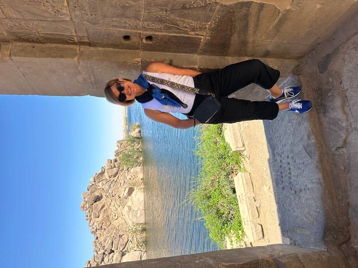 Woman leaning against ancient temple doorway overlooking Nile with rocky island.