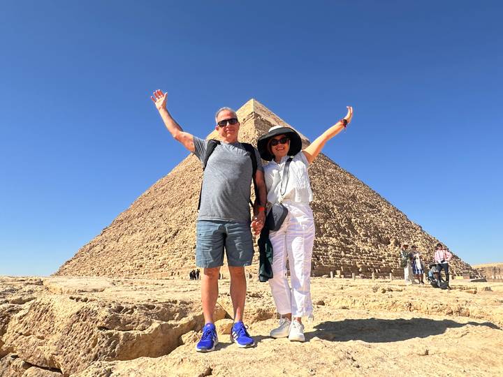 Happy couple raising arms in front of Pyramid of Khafre under deep blue sky.