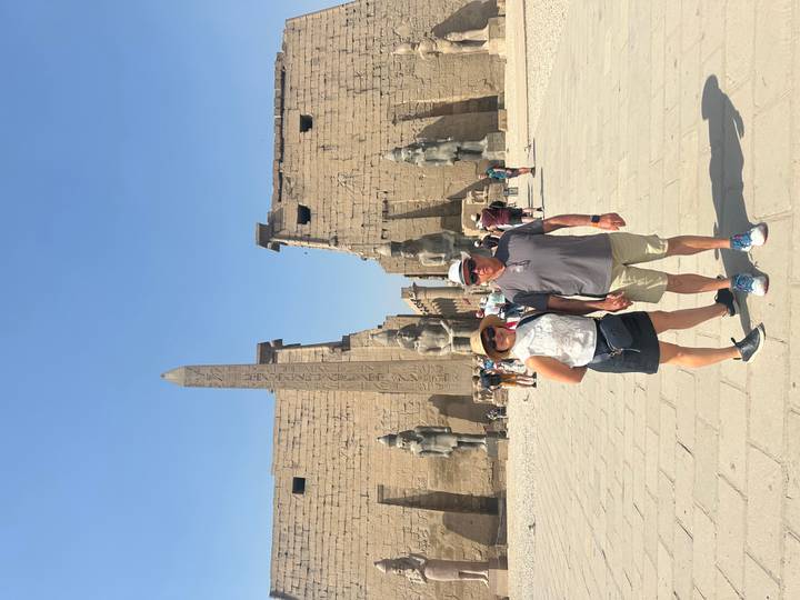 Travelers standing before giant statues and obelisk at Luxor Temple entrance.