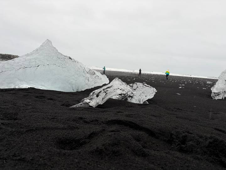 Large blue ice chunks rest on black volcanic sand as visitors explore Iceland’s Diamond Beach.