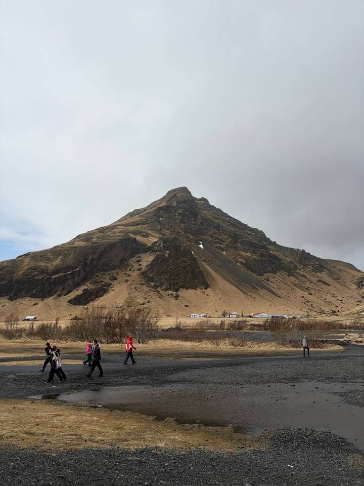 A steep, dark mountain rises above a small Icelandic settlement under moody skies.