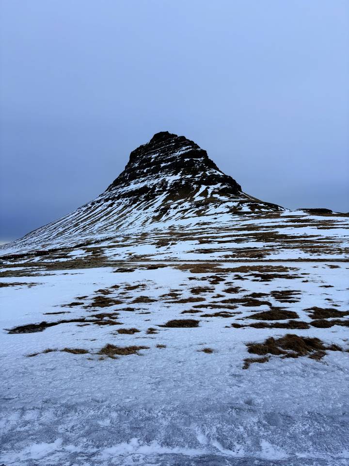 Snow-striped Kirkjufell mountain rises above a windswept icy plain.