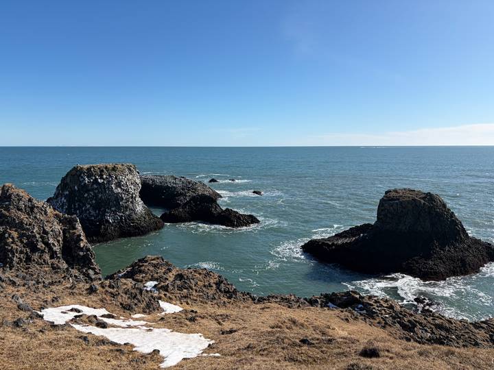 Basalt sea stacks and arches rise from a calm blue North Atlantic beneath clear skies.