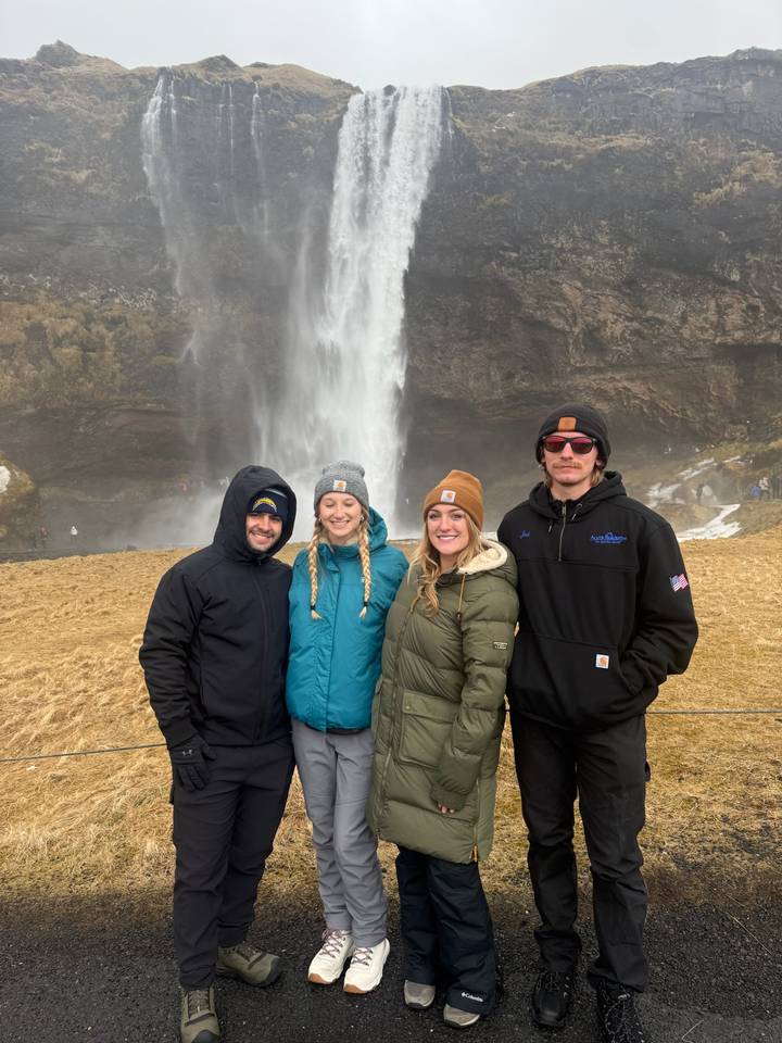 Four friends pose warmly in front of the misty cascade of Seljalandsfoss in winter.