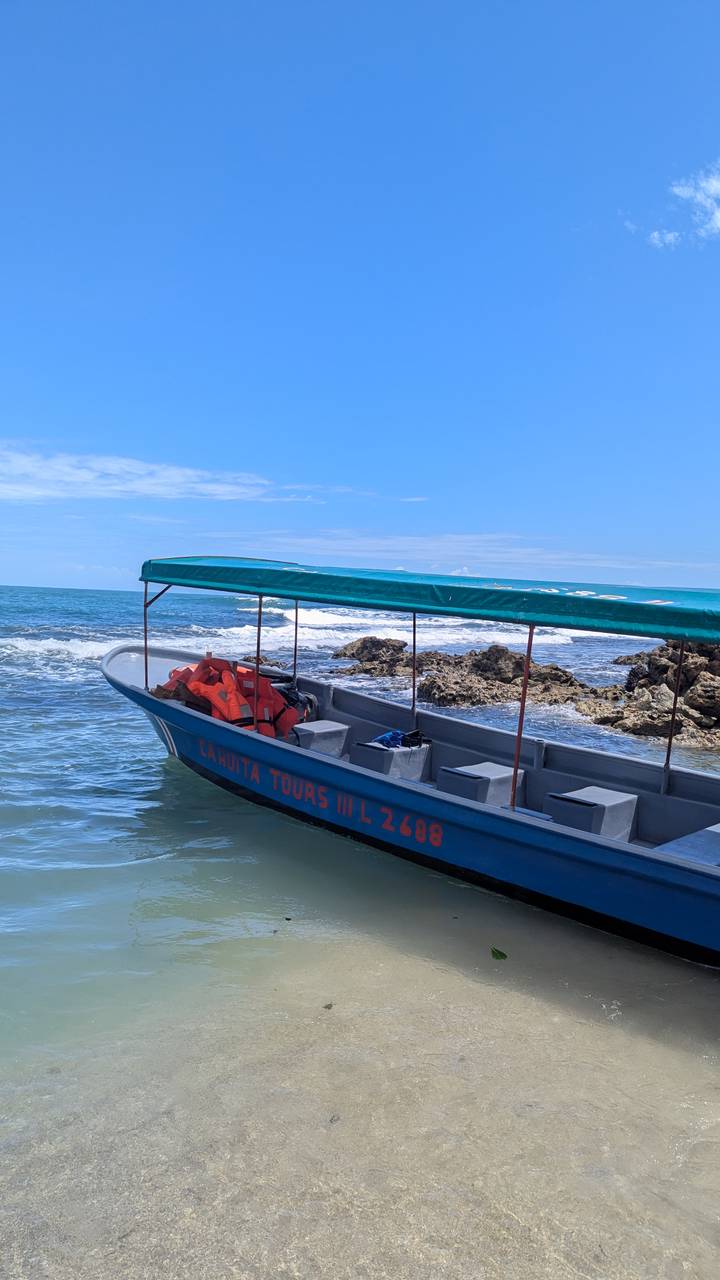 A small tour boat with life jackets waits beside rocky Caribbean shoreline under blue skies.