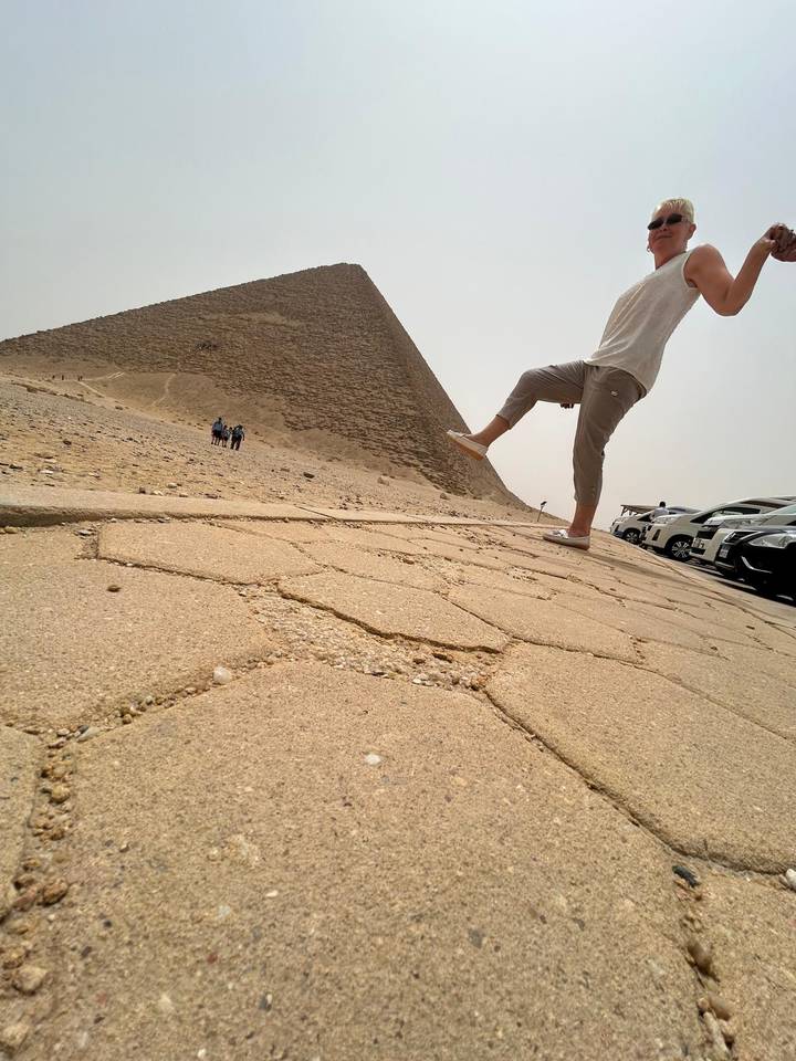 Playful forced-perspective shot of a visitor 'kicking' the Bent Pyramid on a hazy day.