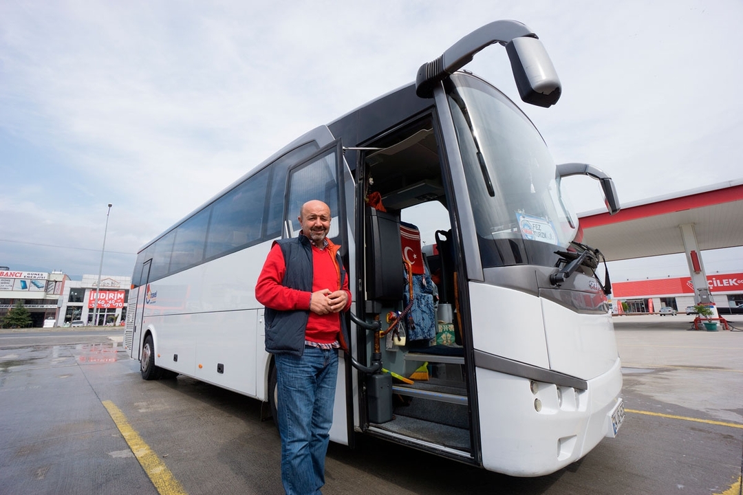 Person posing next to a tour bus in a parking lot.