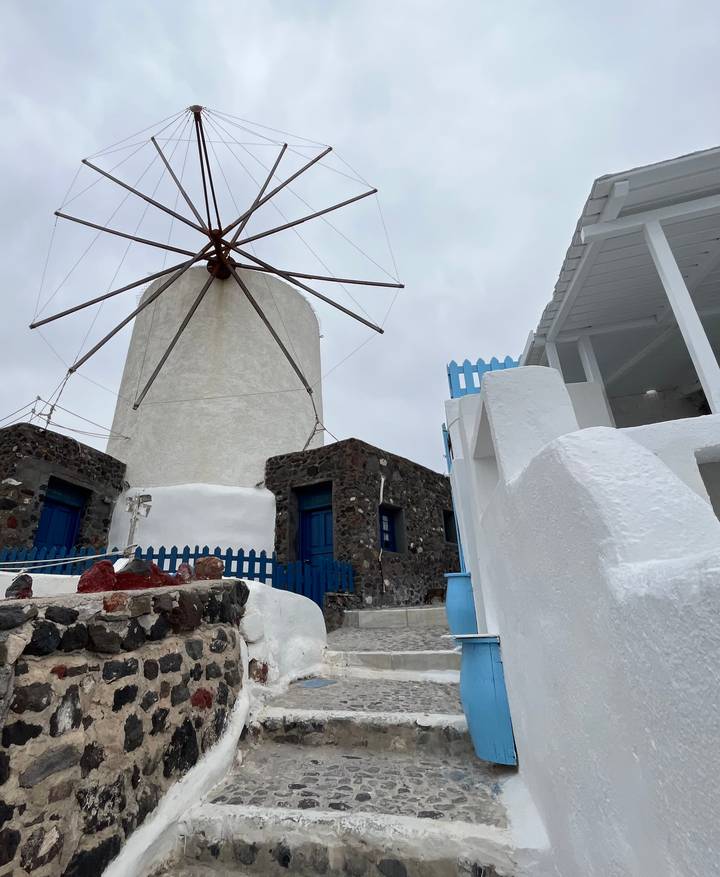 Traditional white windmill and stone house with blue doors on an overcast Greek island day.