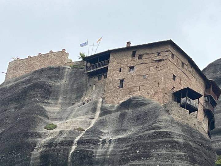 Stone monastery clings to dramatic grey cliffs of Meteora under hazy skies.