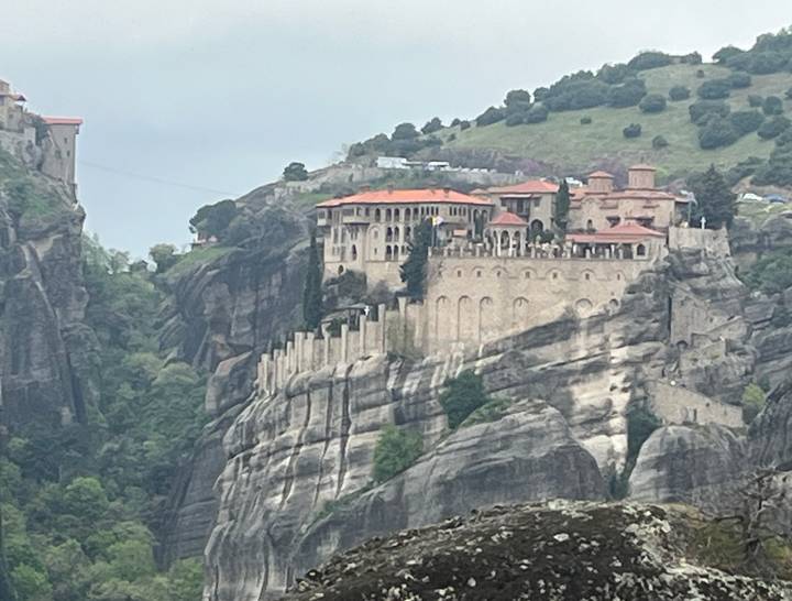 Distant view of fortified Meteora monastery perched atop sheer rock cliff.