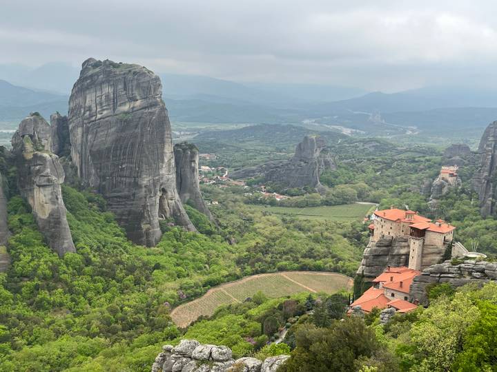 Panoramic aerial view of towering Meteora rock pillars rising above green valley and villages.