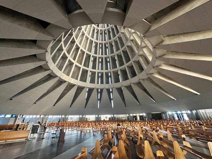 Sweeping interior of a modern circular basilica with soaring concrete ribs and wooden pews.