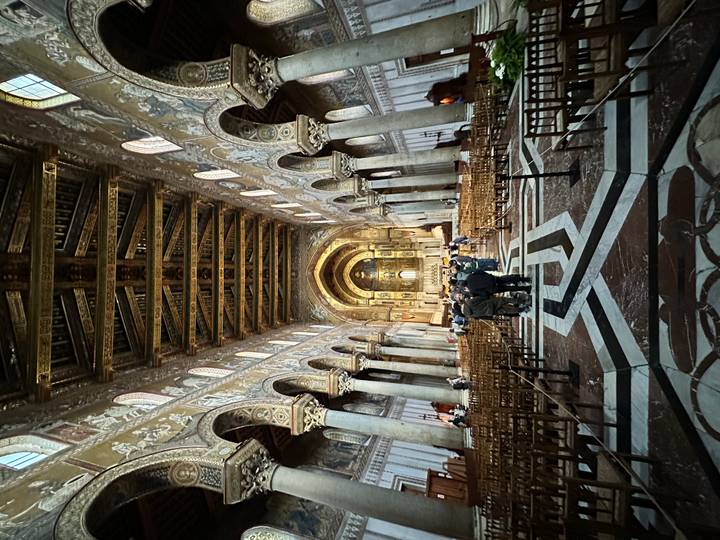 Ornate nave of a grand cathedral lined with mosaics, arches, and marble floor patterns.